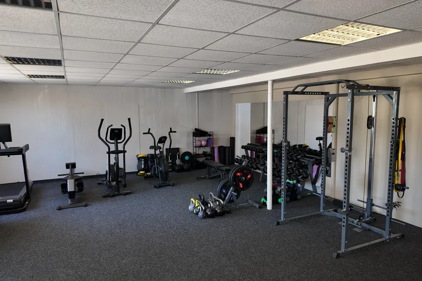 Běžecký pás, eliptické trenažéry, činky a posilovací klec v prostoru fitness